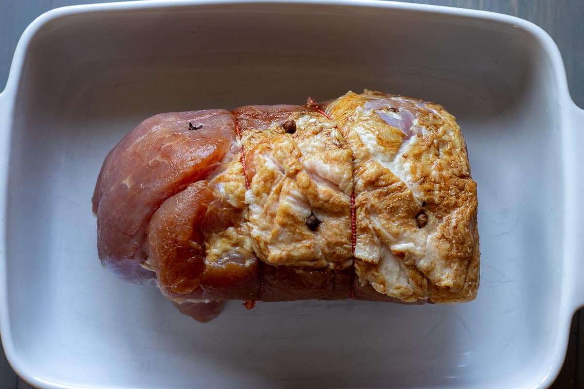 uncooked ham is scored with a sharp knife and placed in a baking dish