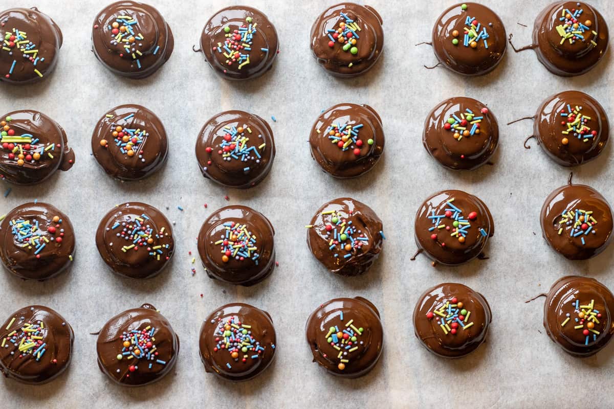 Chocolate covered oreos are placed on a baking sheet and topped with sprinkles.