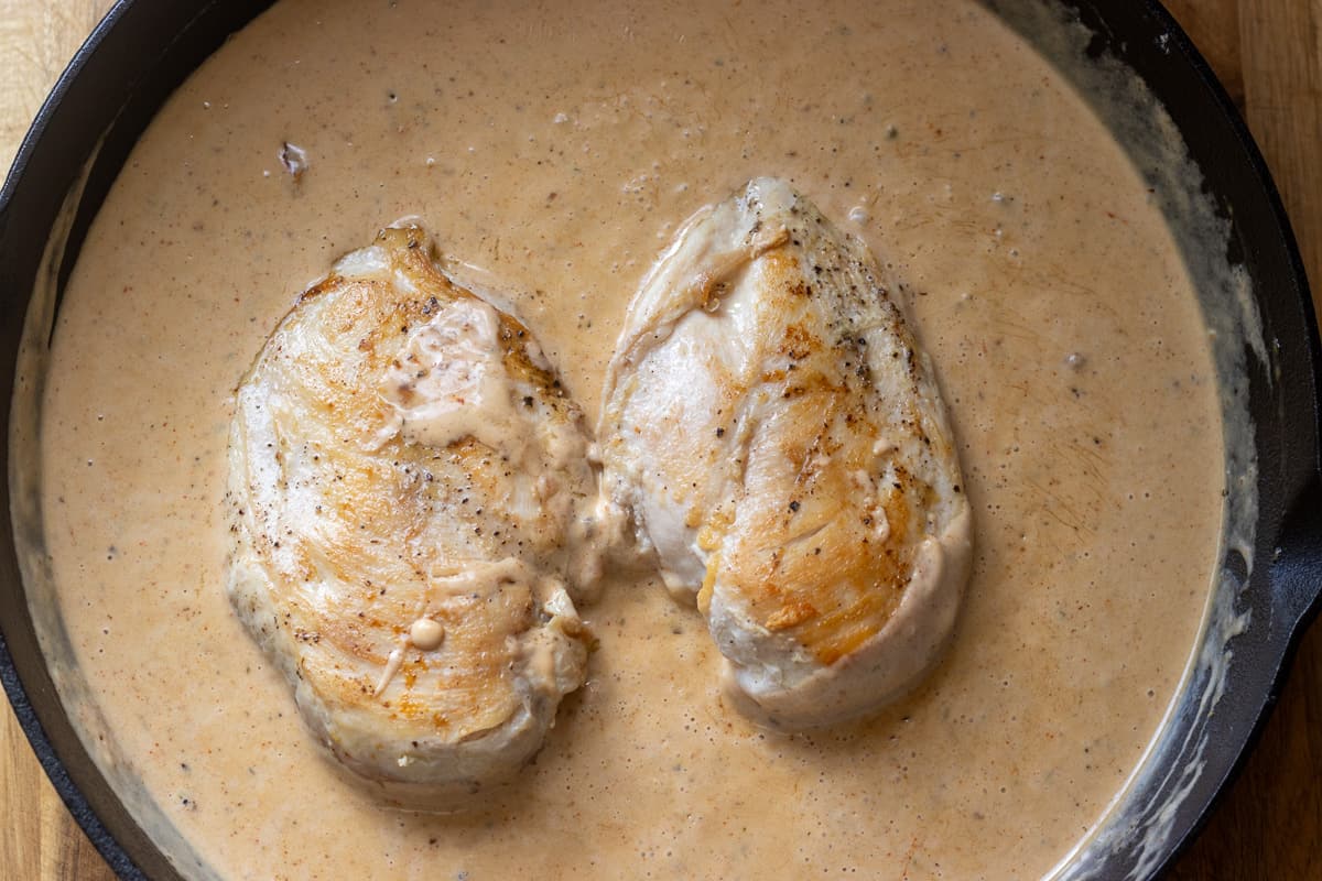 2 seared chicken breasts are placed in creamy sauce