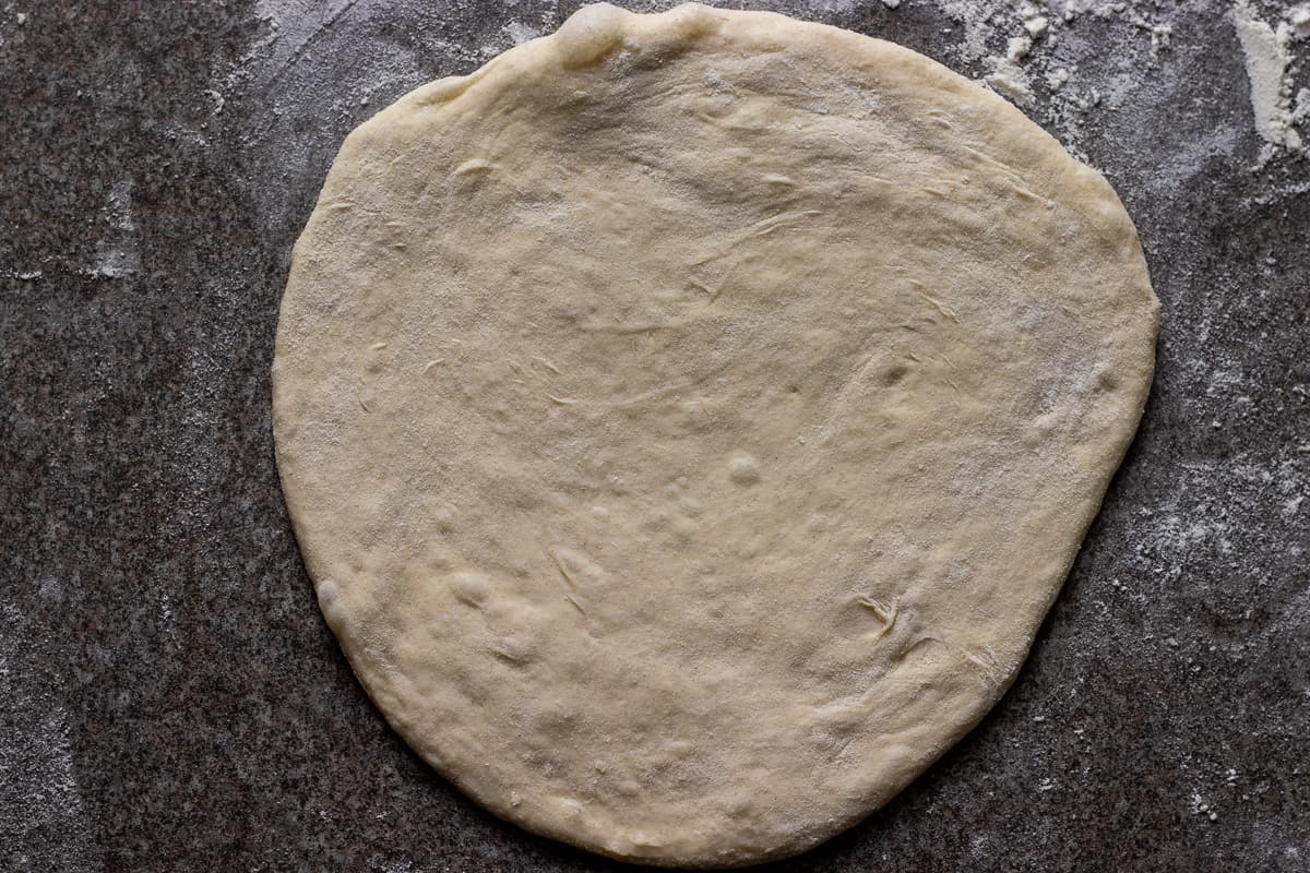 A dough ball is rolled out into a small circle.
