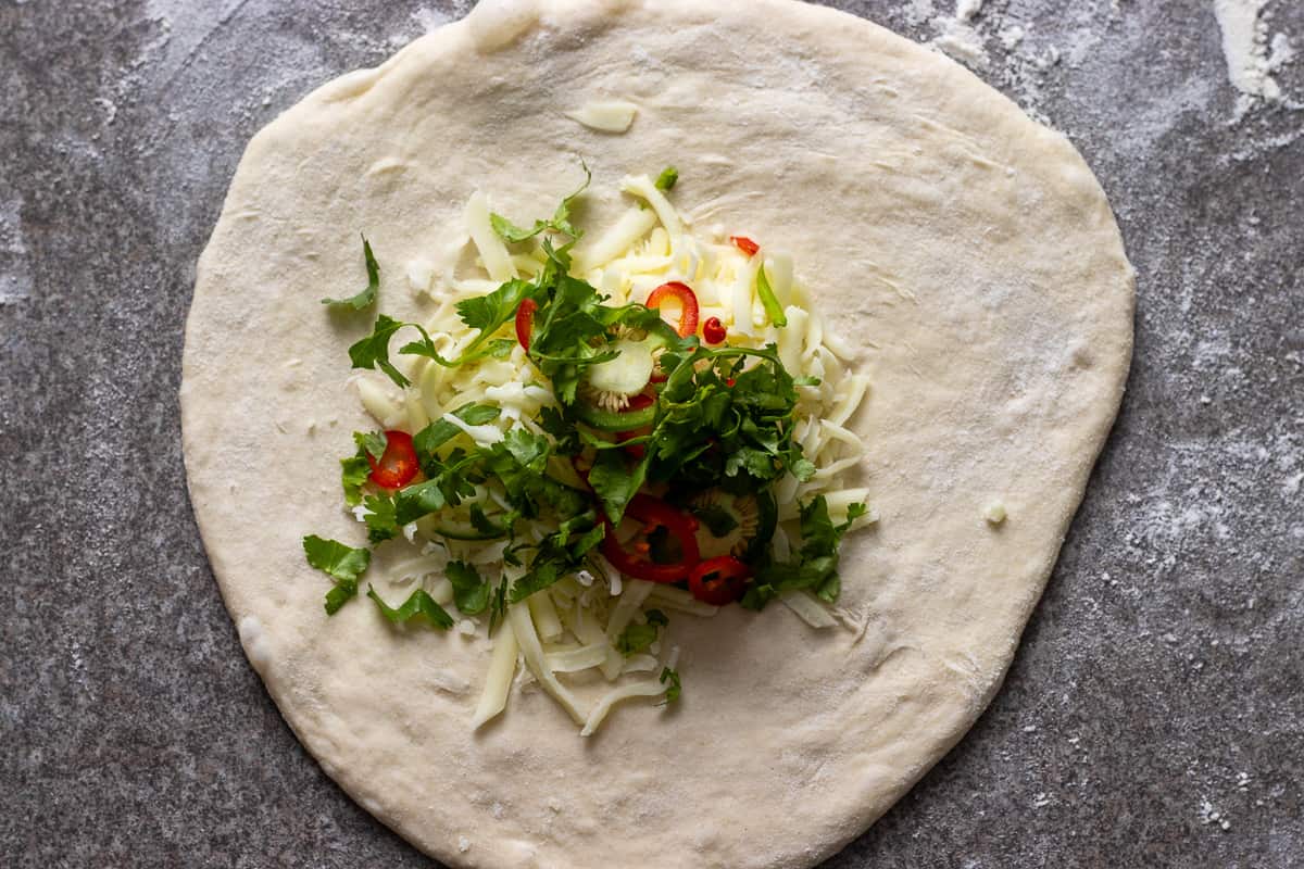 Grated cheese, coriander, and chilies are placed in the centre of the dough circle.