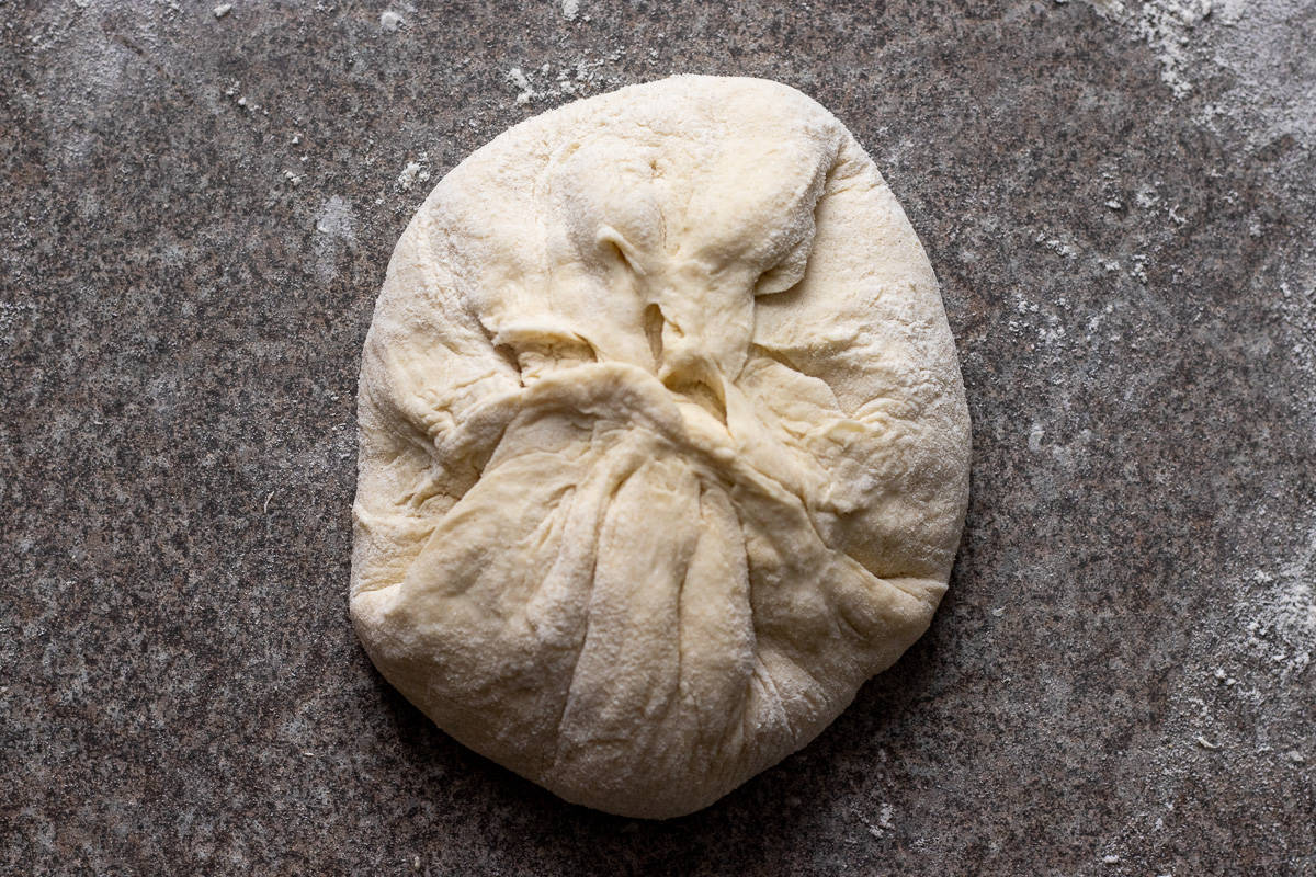 The sides of the dough is pulled up to seal and shape into a ball.