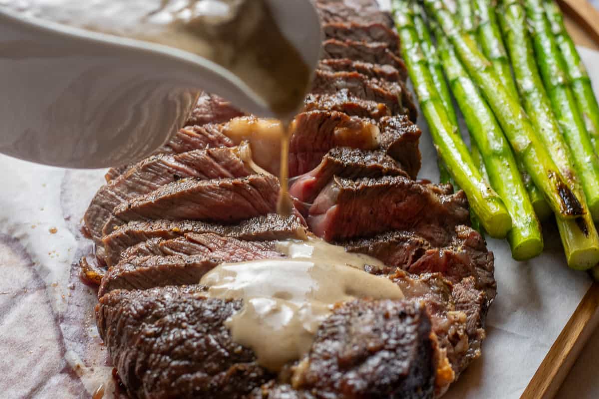 pouring creamy mushroom sauce on grilled steak