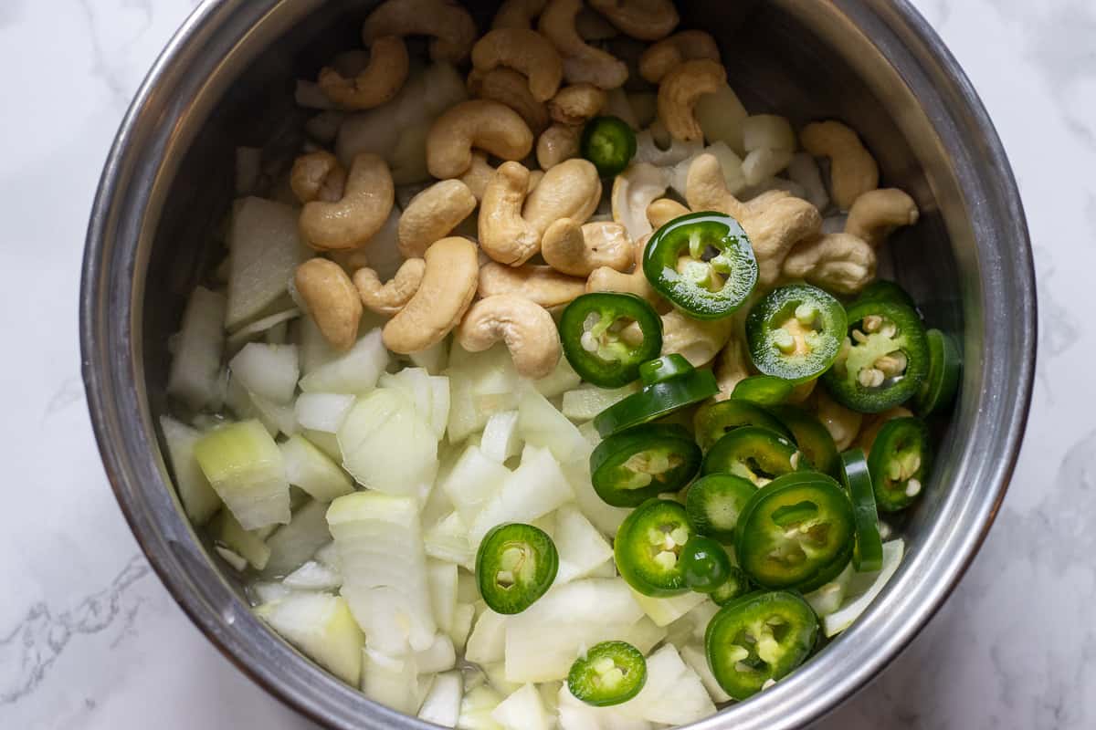 roughly chopped onions and chili are placed in a pan along with cashew nuts