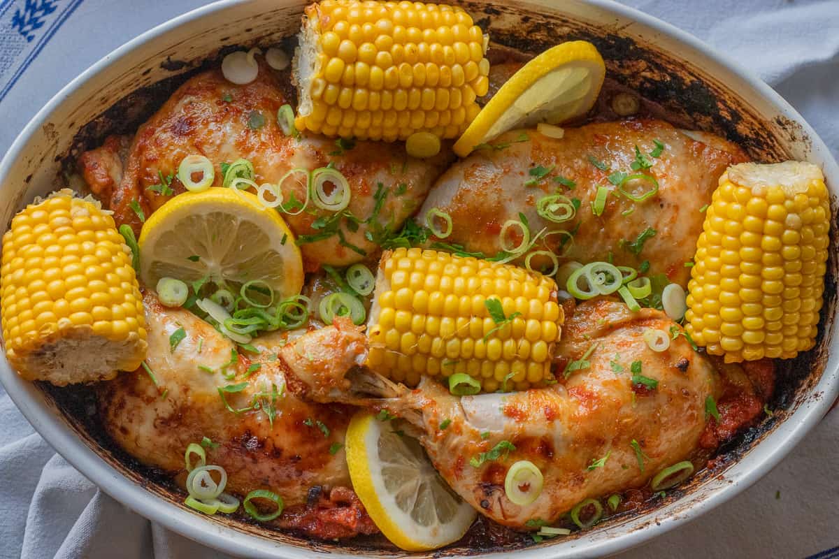 chicken pieces are baked until golden brown and served with corn on the cobs