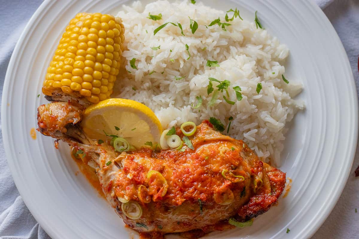 homemade peri peri chicken served with rice and corn on the cobs

