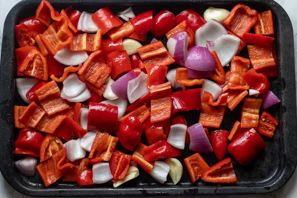 red onion, red pepper, garlic, and chili are placed on a baking sheet
