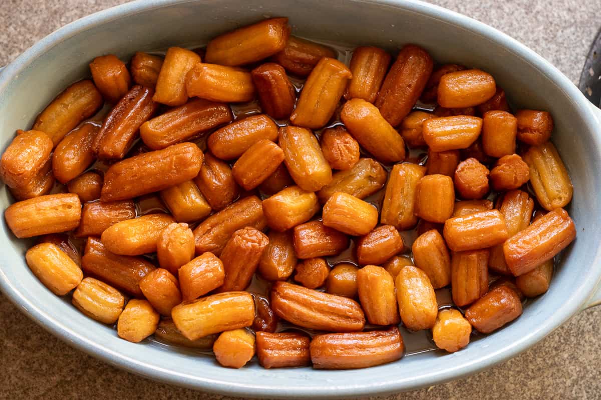 fried dough balls are trandseffer into a bowl filled with syrup