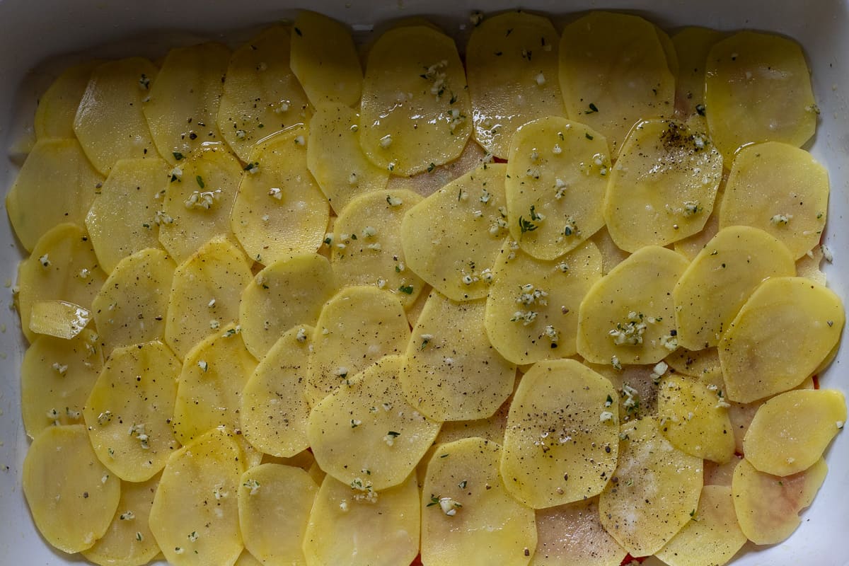 sliced potatoes are layered over sliced tomatoes