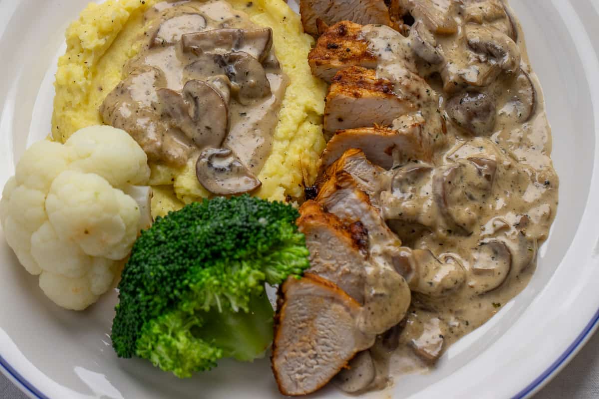 turkey tenderloin is sliced and served wit mashed potatoes, mushroom sauce, and veggies
