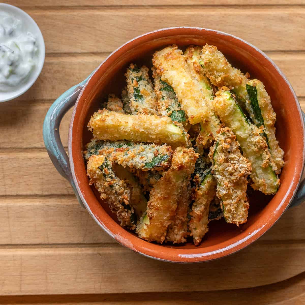 A bowl of fried zucchini sticks with a side of ranch dressing