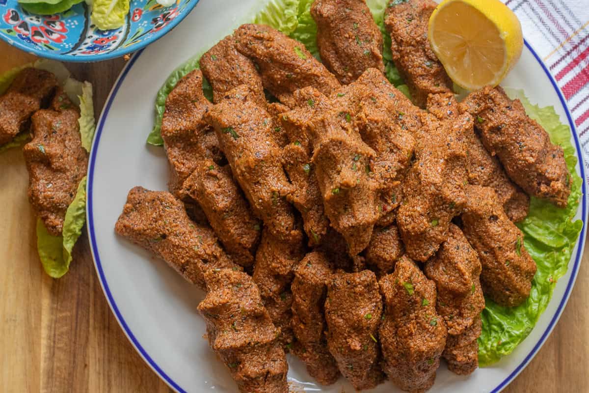 Cig Kofte served with lettuce and lemon on a plate.