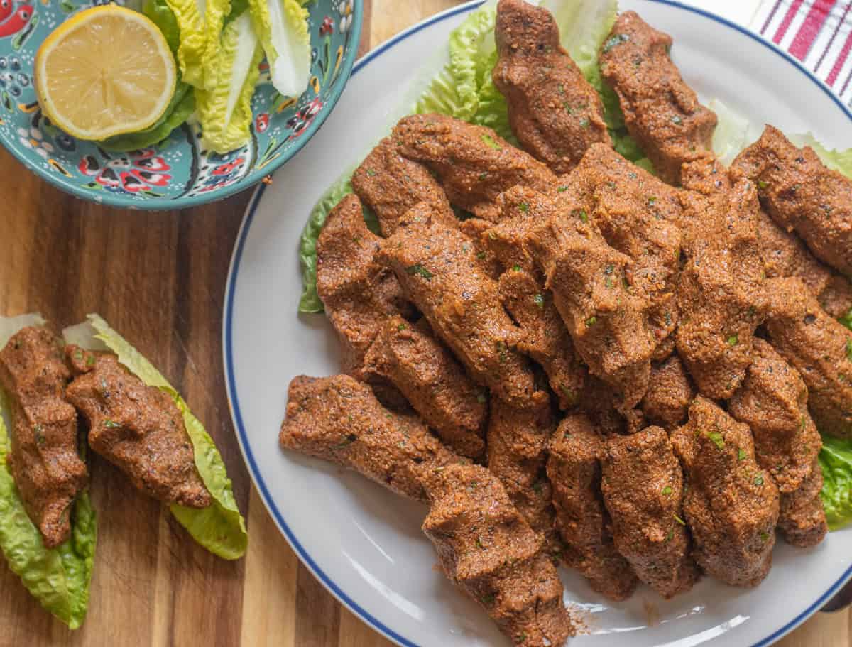 Cig kofte patties are served on a plate with half a lemon and lettuce leaves.