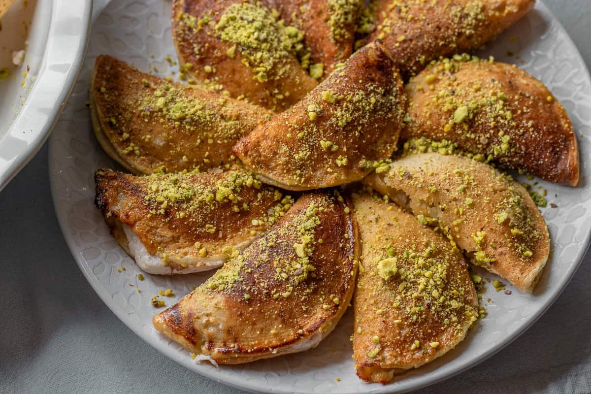 10 pieces of katayef layered on a plate and sprinkled with pistachio nuts