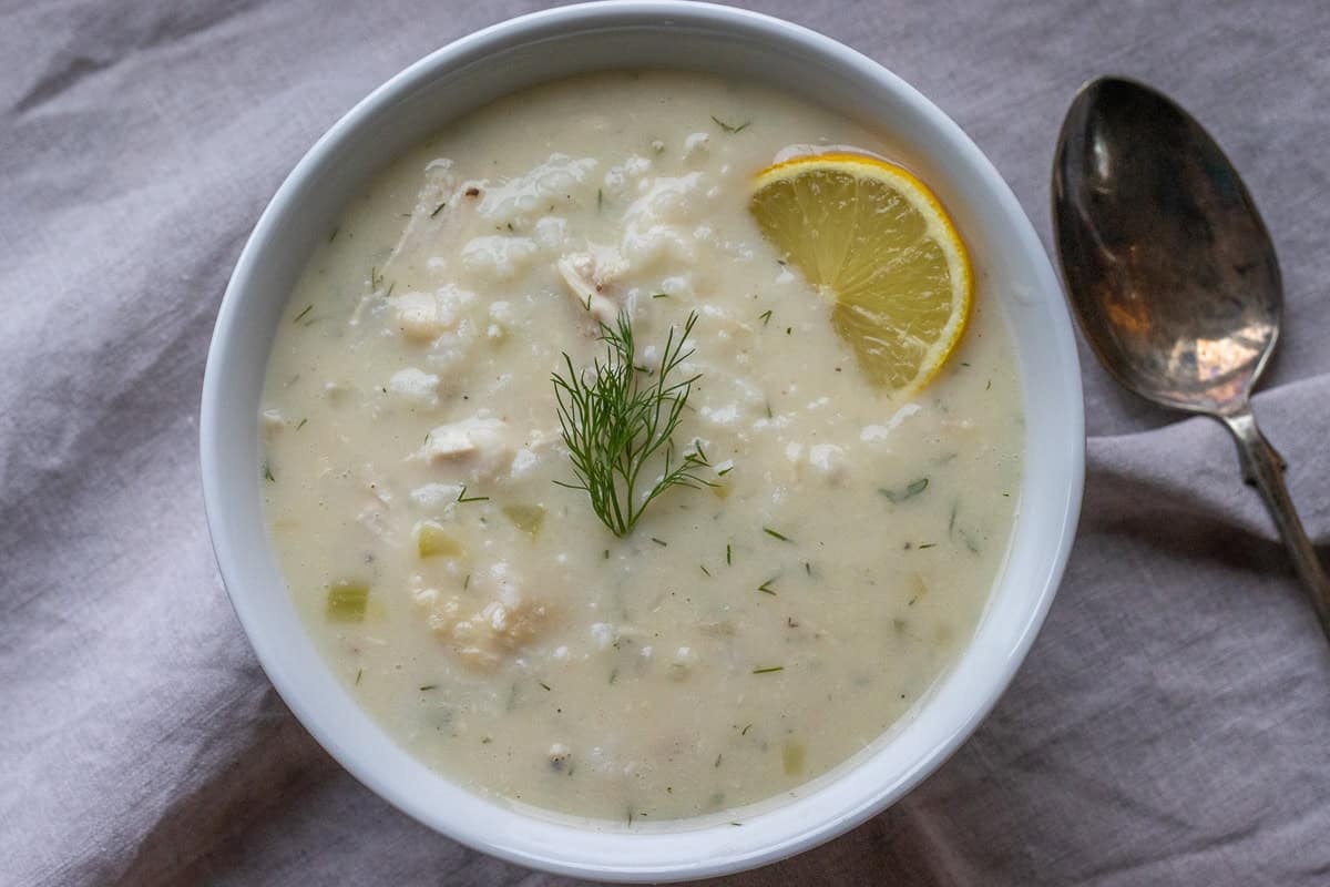 Greek lemon chicken soup served ina white bowl with a silver spoon next to it.
