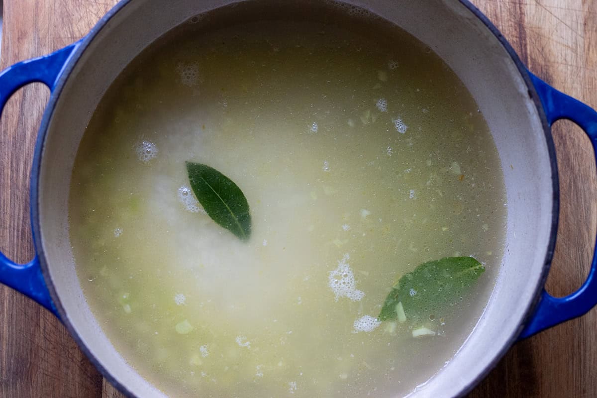 Stock, rice, seasoning, and bay leaves are added to the pot.