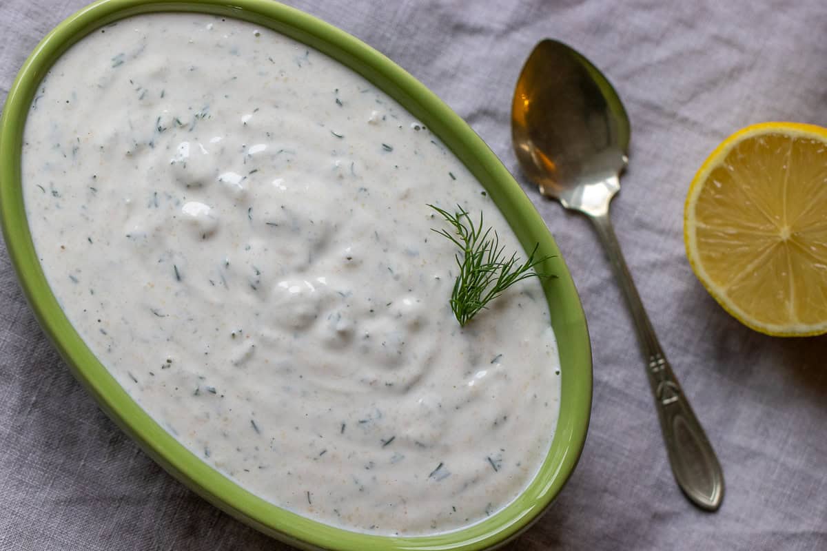 shawarma white sauce in a plate served with a spoon and half lemon