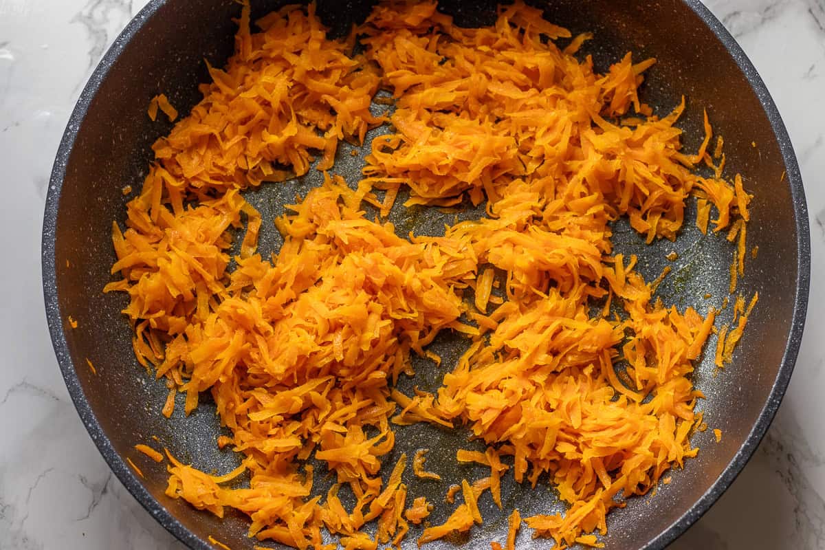 sautéing grated carrots in a pan with olive oil