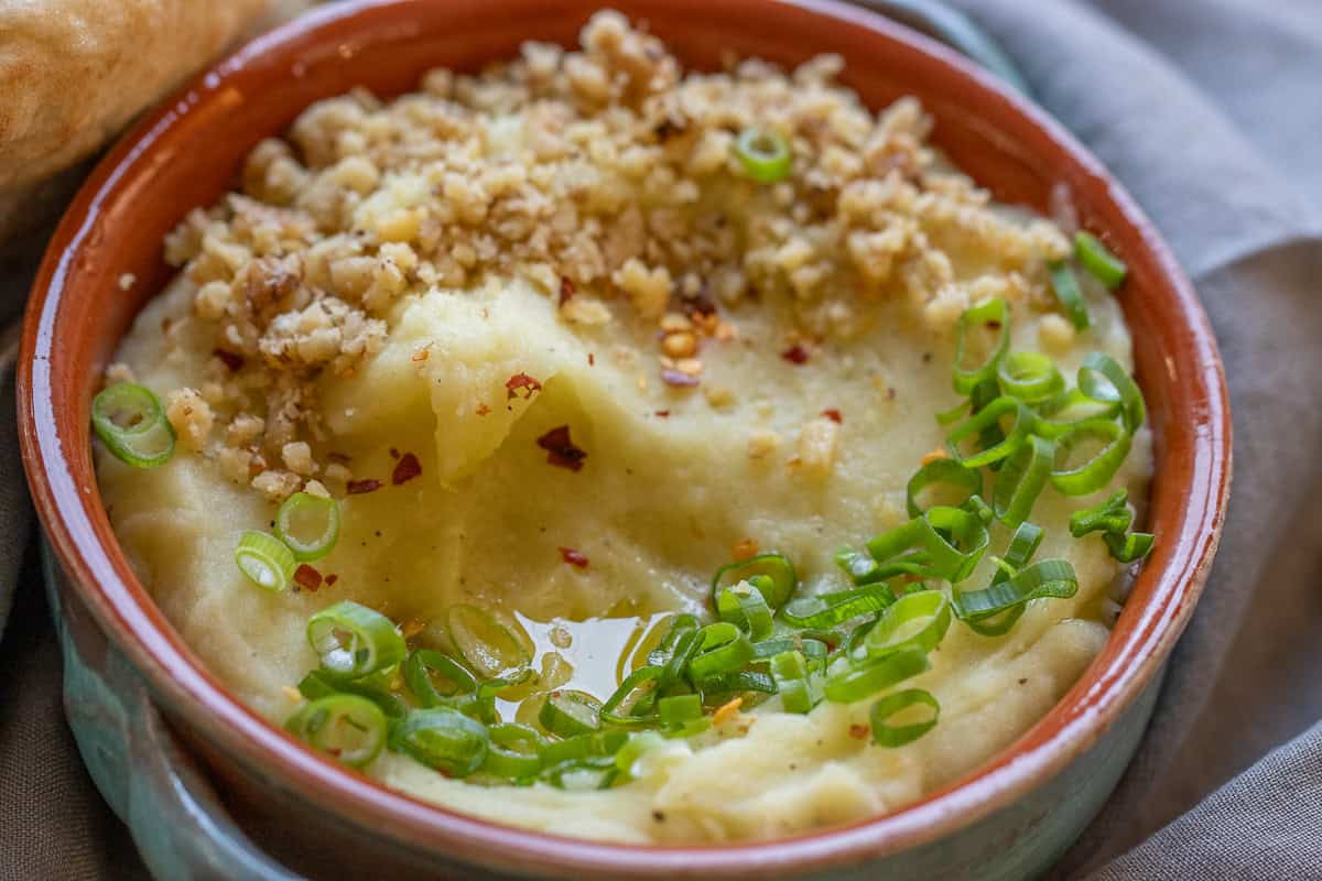 greek potato dip garnished with crushed nuts and green onions