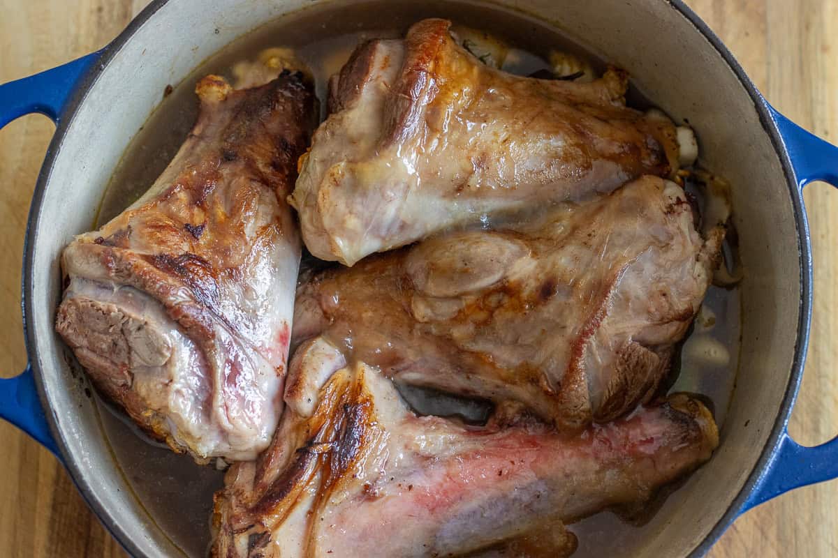4 pieces of lamb shanks are placed in a pot over the sautéed vegetables