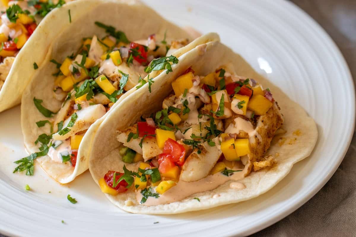 3 pieces of fish tacos with mango salsa served on a plate
