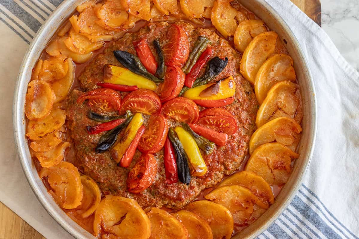 meat patty placed in the middle of a tray, and covered with vegetables and potato slices