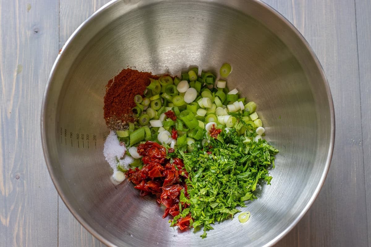 finely chopped spring onions, fresh herbs, and sun dried tomatoes are placed in a bowl