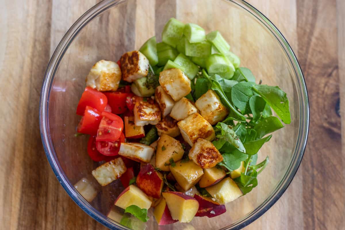 tomatoes, cucumbers, halloumi, arugula, and peaches are placed in a bowl