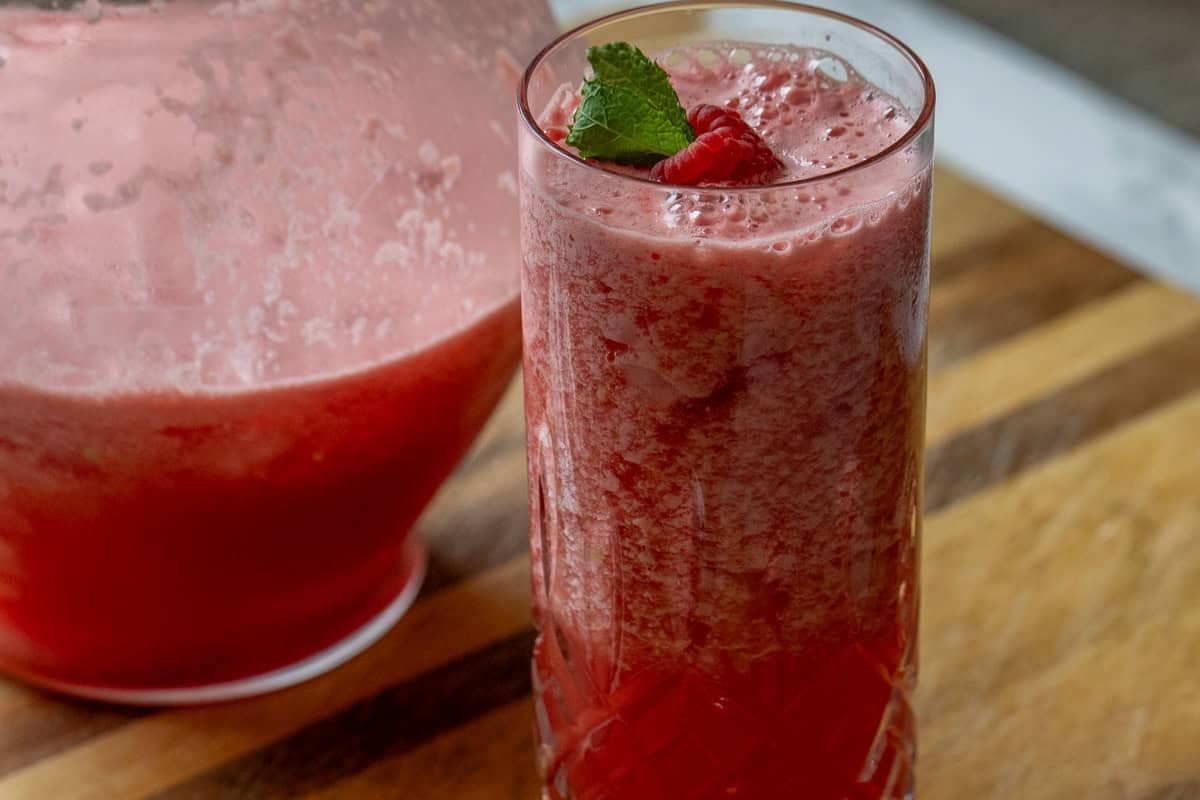a glass of watermelon cocktail garnished with raspberry and mint leaves
