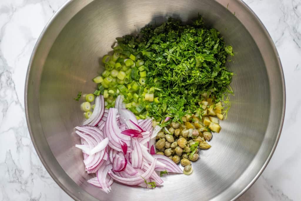 red onions, spring onions, fresh herbs, capers, and pickled cucumbers are placed in a bowl