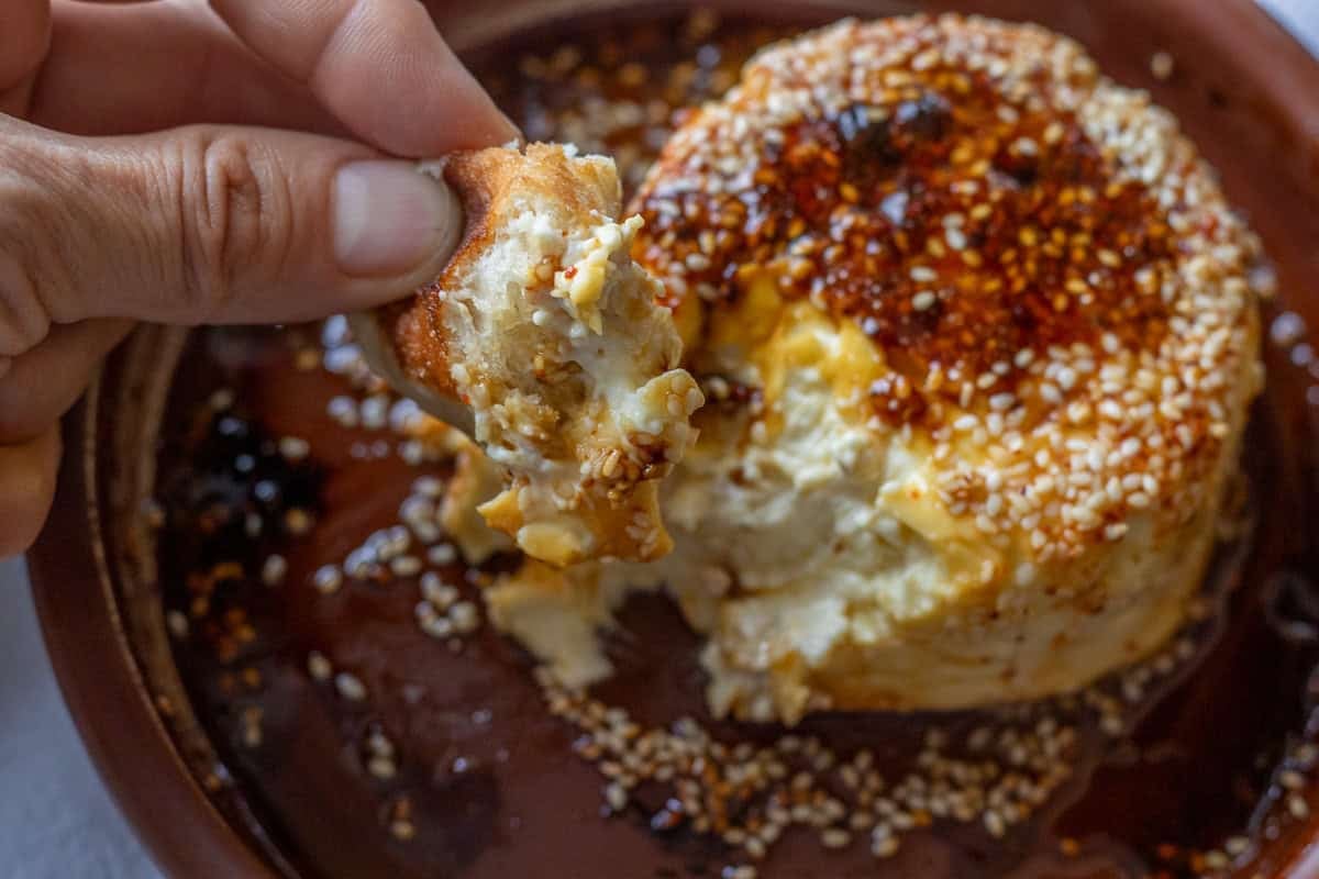 dipping a piece of bread to baked feta wit honey